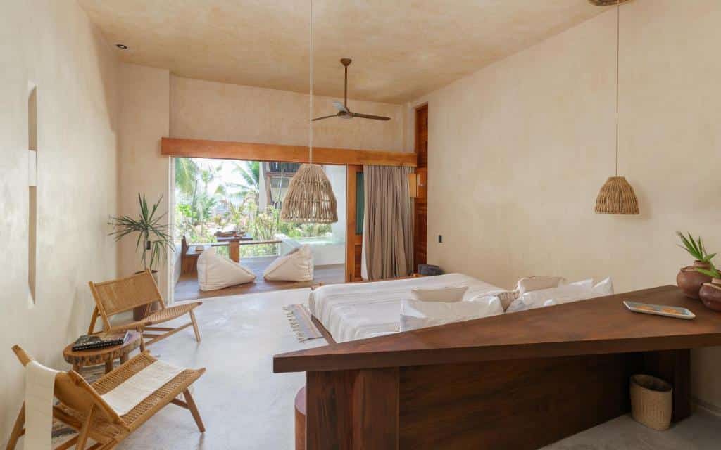 Suíte Júnior do Hotel Ma'xanab, de 72 m², com cama de casal, cadeiras artesanais ao lado e uma varanda com chão de madeira, puffs, mesa e hidro com vista para a natureza