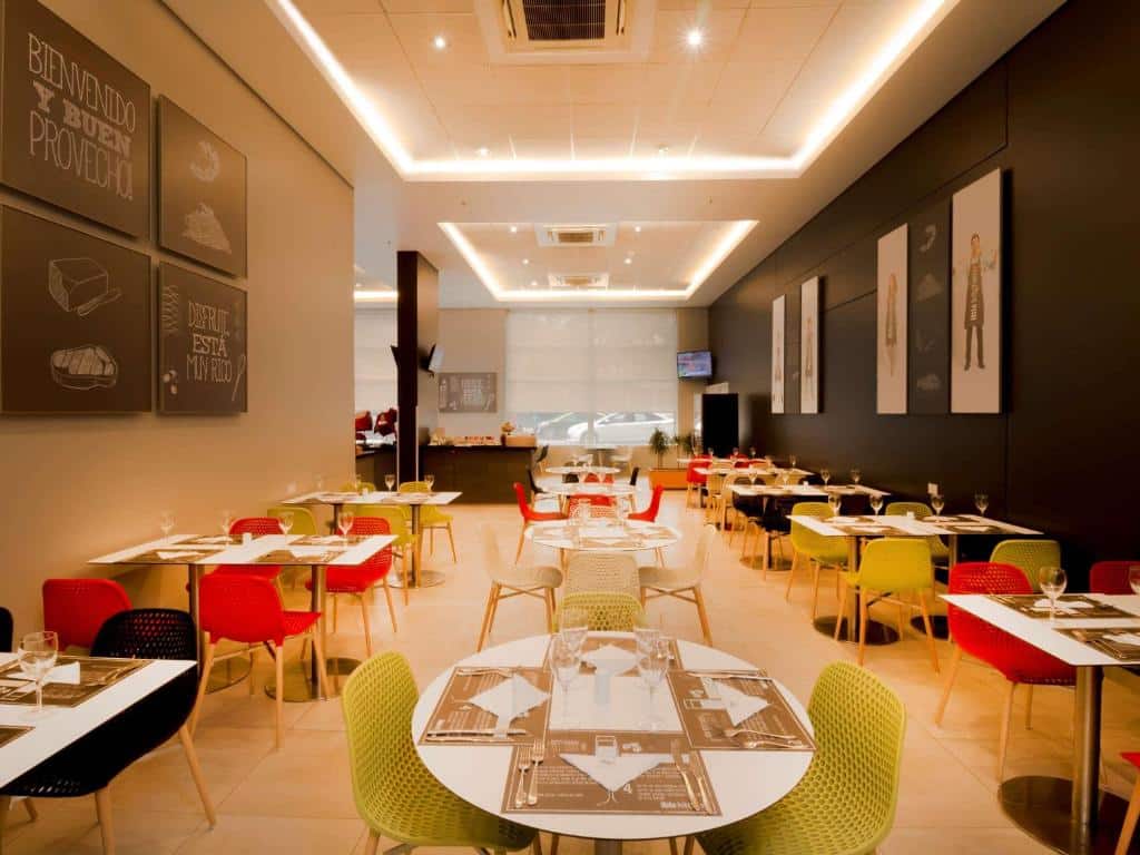 Área de refeições do ibis Santiago Providencia com mesas de madeira, cadeiras coloridas, com alguns quadros nas paredes, para representar hotéis Ibis em Santiago do Chile