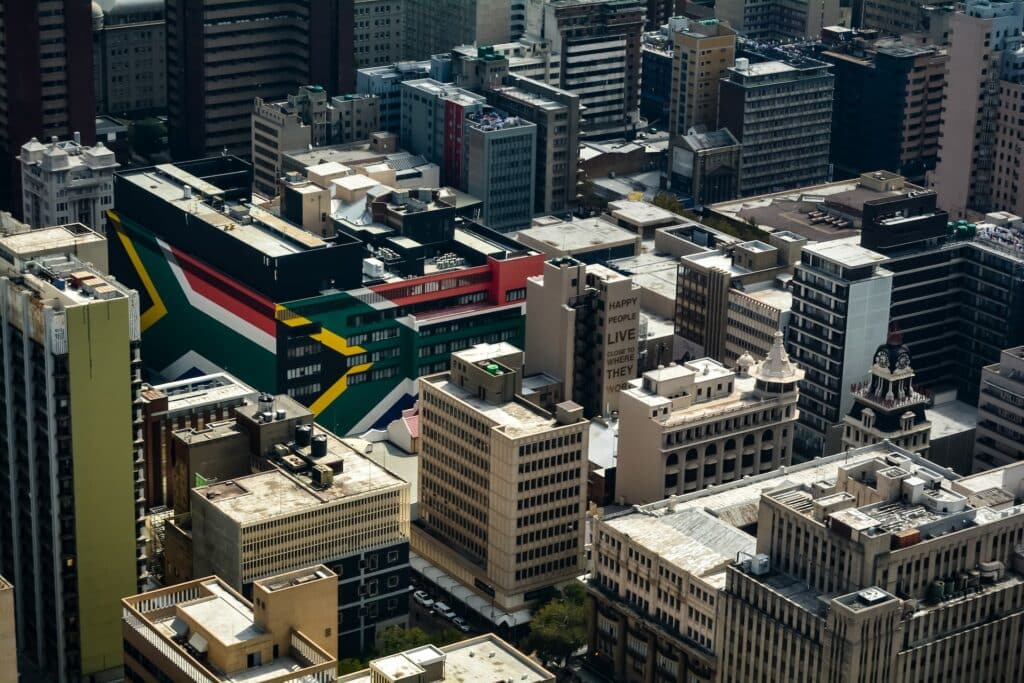 Centro da cidade de Joanesburgo para ilustrar o post sobre chip de celular para Johanesburgo. Há diversos prédios, e um deles chama a atenção por ter a bandeira da África do Sul estampada na fachada. - Foto: Jacques Nel via Unsplash