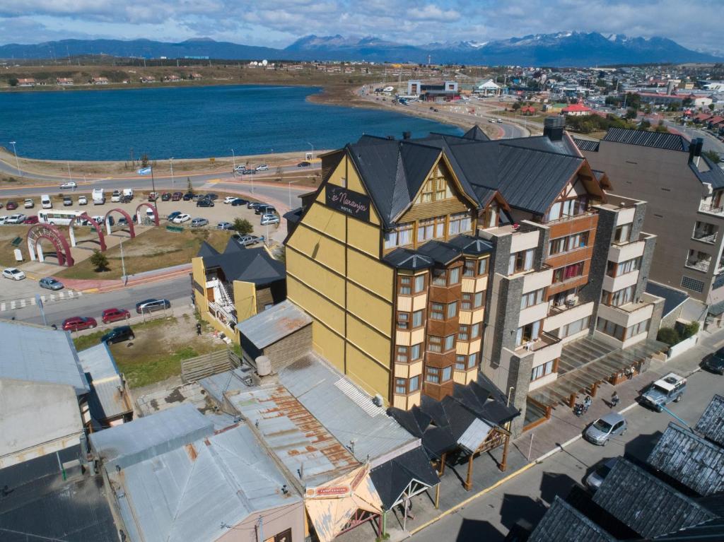 vista aérea do hotel Los Naranjos com um prédio em construído em estilo bechamel e várias outras casas e prédios ao redor. Ao fundo é possível ver o lago de Ushuaia