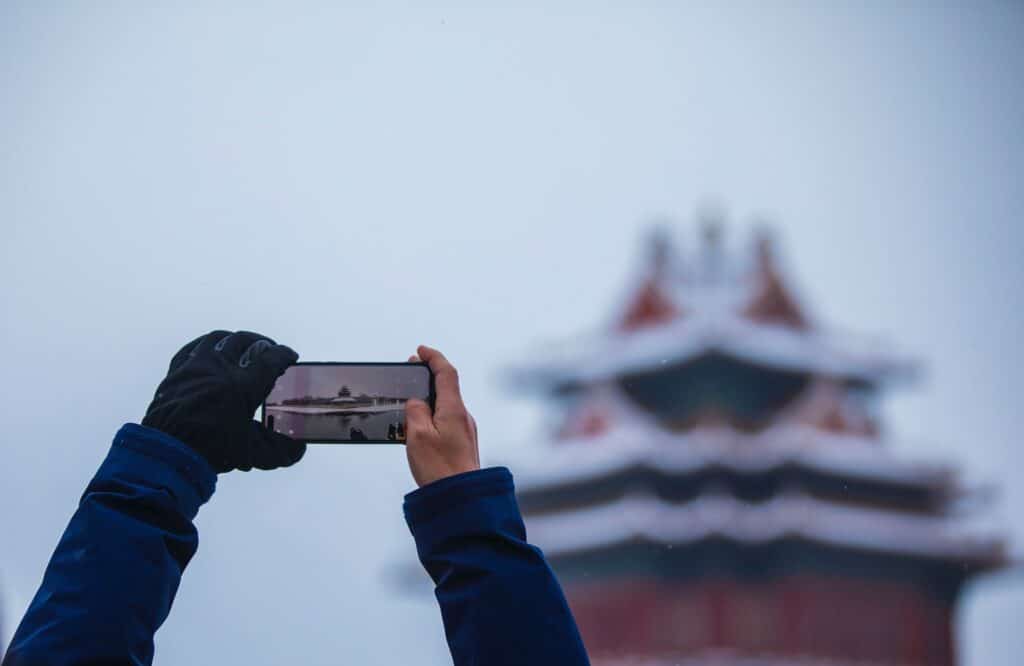 Duas mãos masculinas segurando um celular na horizontal para fotografar um dos templos em Pequim