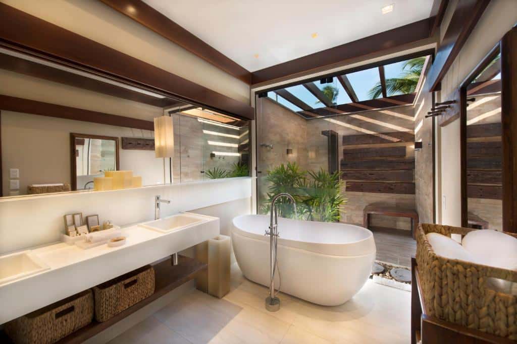 Banheiro do NANNAI Muro Alto em que o box tem um teto de vidro, uma banheira oval, duas pias, um amplo espelho e alguns itens de higiene