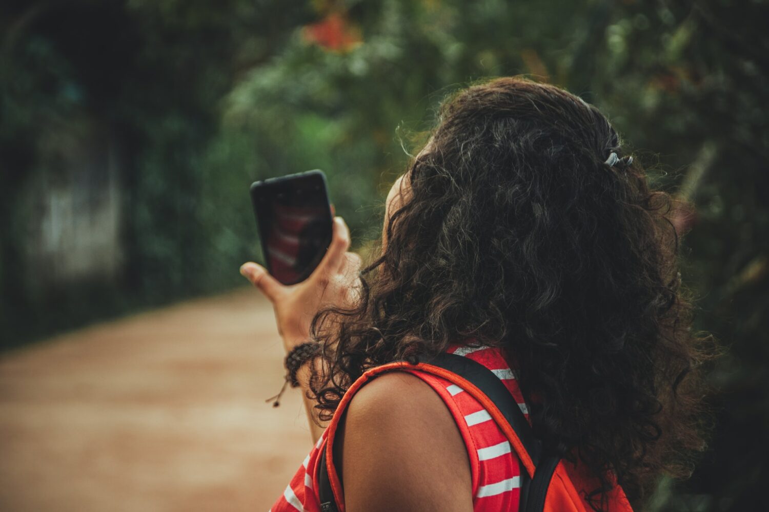 Uma mulher de cabelos enrolados e camiseta vermelha segurando o celular perto de um local com árvores por perto, para representar chip celular Sri Lanka