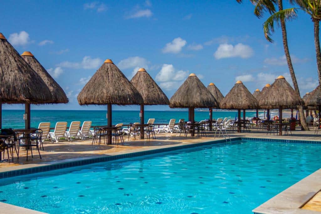Piscina do Ocaporã Hotel All Inclusive com um deck virado para a praia com espreguiçadeiras e guarda-sóis em formato de oca, para representar resorts em Muro Alto