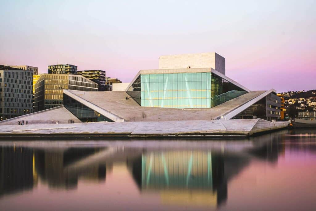 vista da Ópera de Oslo, uma estrutura moderna com ângulos retos e muito vidro refletindo nas águas de um lago a frente, para ilustrar o post de chip celular Noruega