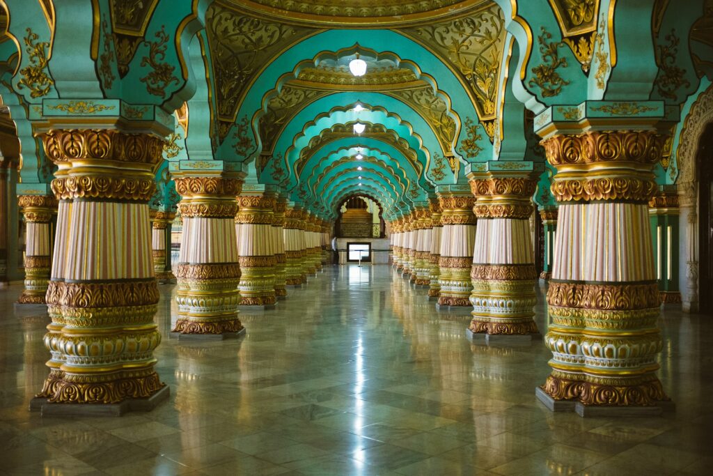 interior do Palácio Mysore, em Mysuru, com colunas ricamente decoradas em dourado e verde esmeralda, com fundo branco e chão de mármore brilhoso, há também muitos detalhes em cada canto, para ilustrar o post de chip celular Índia