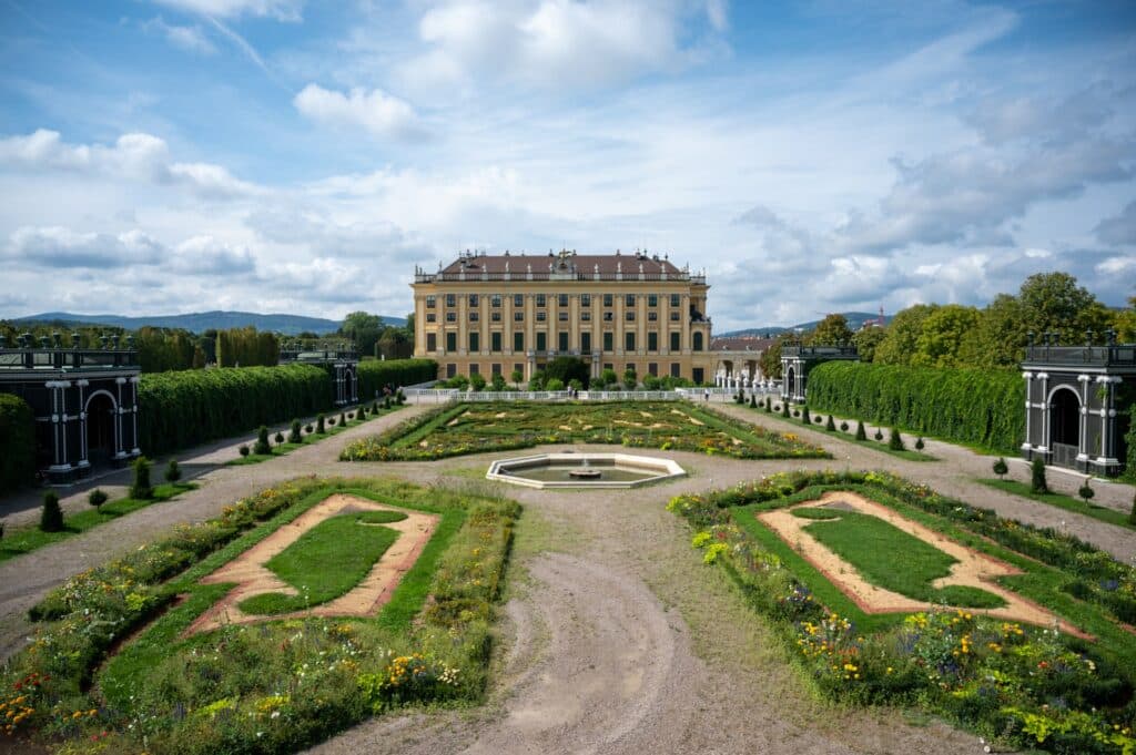 Palácio de Schönbrunn em Viena na Àustria. Grande construção ao fundo com jardim vasto à frente e ao entorno.