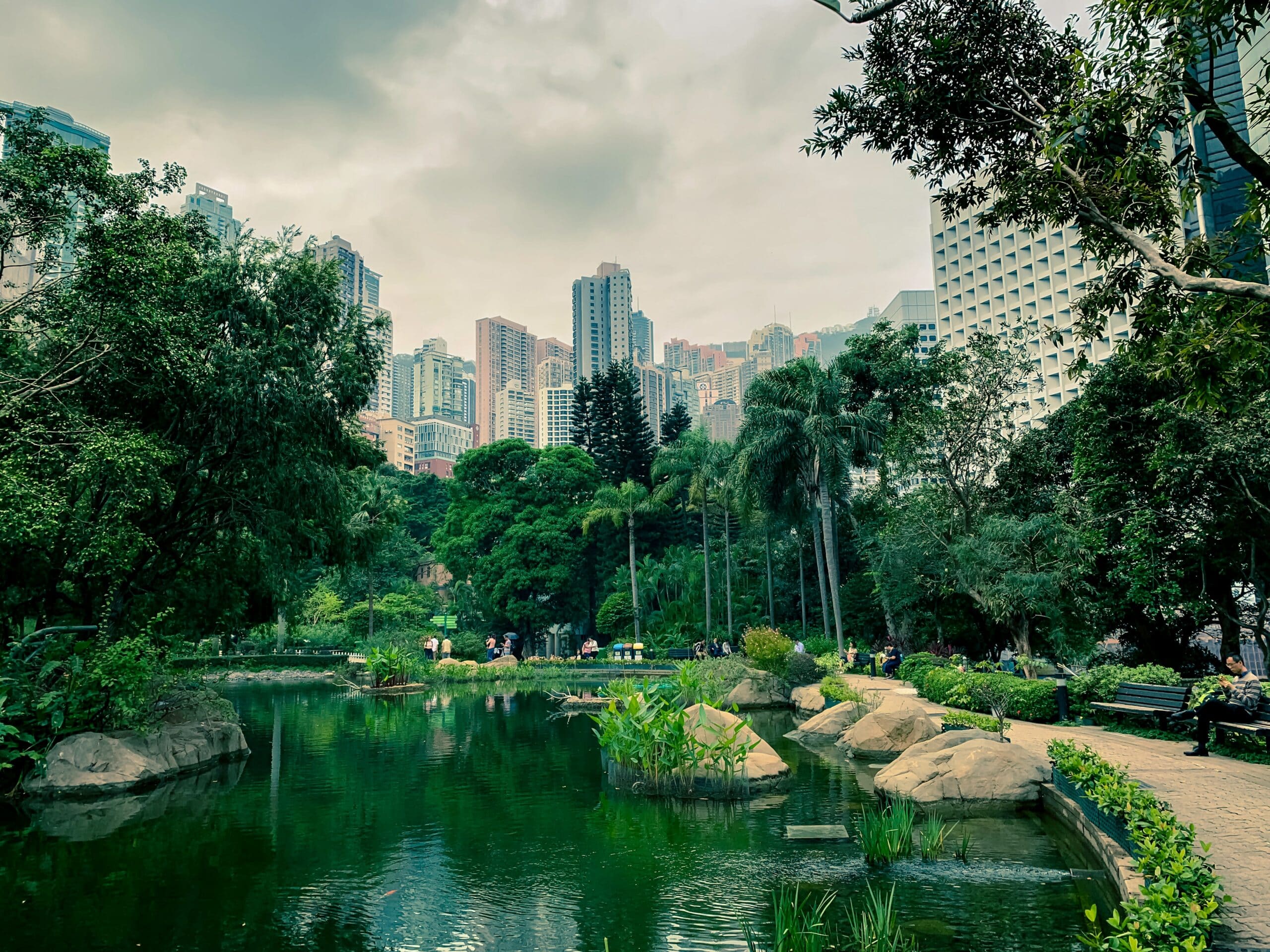 Vista do Parque de Hong Kong durante o dia com um lago a frente, pedras e vegetação em volta.