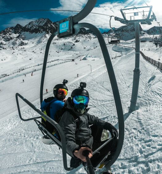 Duas pessoas andando em um teleférico ao redor de bastante neve em uma estação de esqui durante o dia, ilustrando post chip celular Andorra.