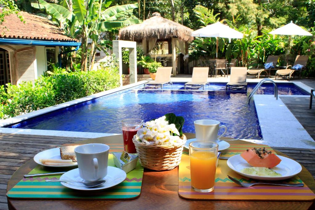 Vista da piscina do Canto do Camburi com café da manhã, e ao fundo, tem piscina e cadeiras perto da piscina. Representa pousadas em Camburizinho.