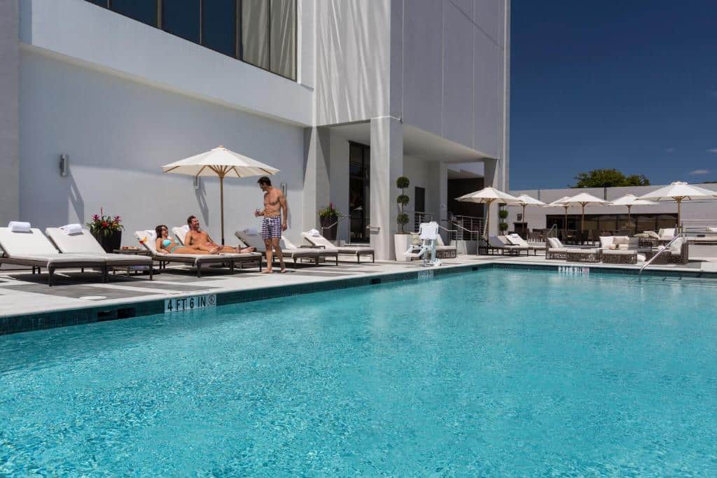 Vista da piscina do EB Hotel Miami Airport durante o dia com cadeiras do lado esquerdo com um casal sentado nelas e um home de pé. Representa Hotéis com cozinha em Miami.