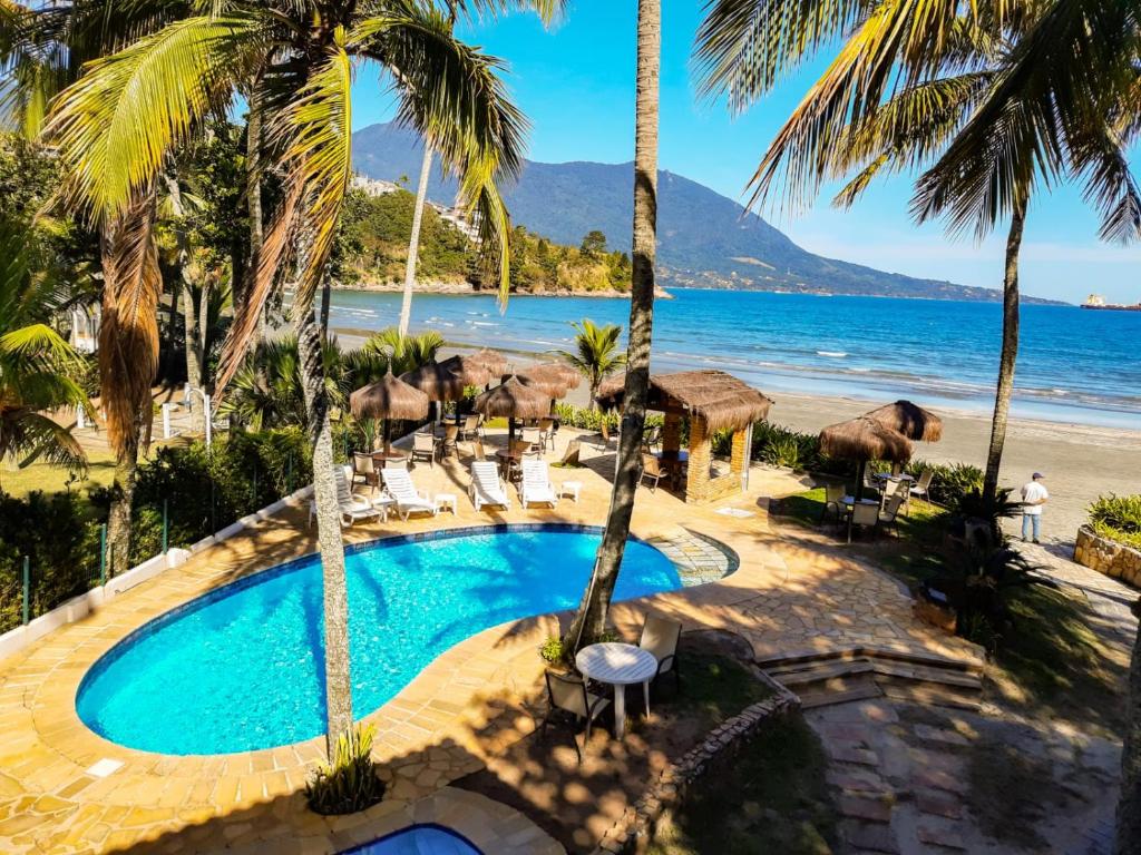Vista da piscina do Barequeçaba Praia Hotel à beira-mar com cadeira em volta, quiosques rústicos e ao fundo a praia. Representa pousadas na praia de Guaecá.