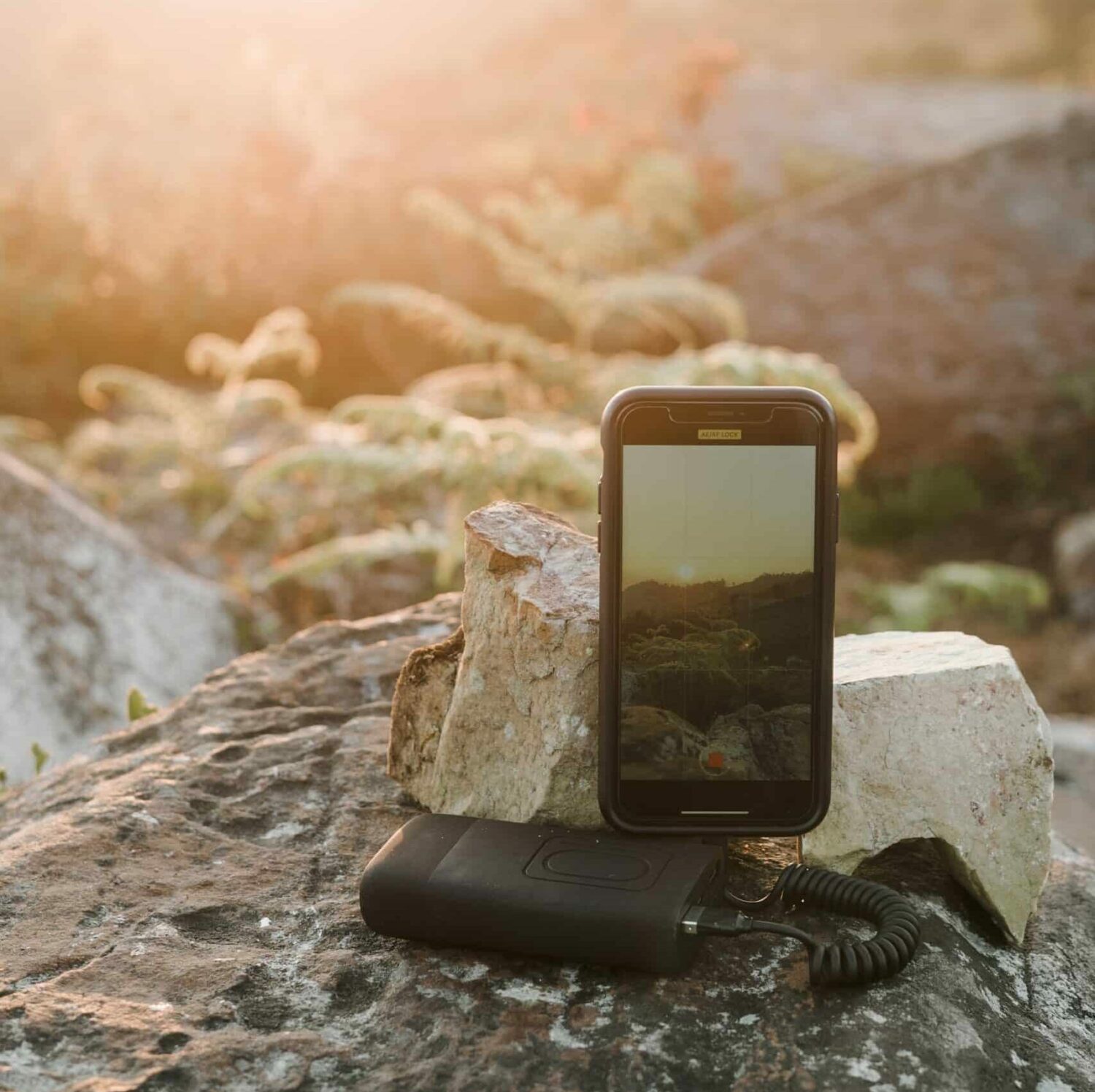 Celular com um aparelho ao lado, em cima de uma rocha e encostado em uma pedra, com paisagem e pôr do sol ao fundo. Imagem para ilustrar o post de chip de celular Nepal