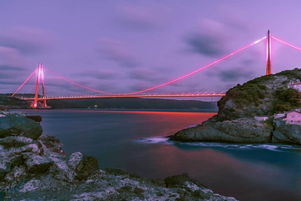 vista noturna em tons de roxo da Ponte Yavuz Sultan Selim, Bósforo, com águas calmas abaixo, rochas e a ponte está iluminada com cores avermelhadas, para ilustrar o post de chip celular Istambul
