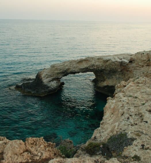vista de uma pessoa em cima da Ponte do Amor, uma estrutura de rocha natural que forma uma ponte com águas cristalinas abaixo e céu azul, para ilustrar o post de chip celular Chipre
