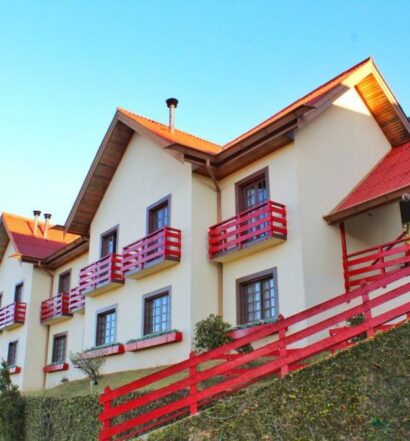 A Pousada AlpenRose, uma construção de dois andares em tom de bege com as sacadas pintadas em vermelho, para representar pousadas baratas em Campos do Jordão