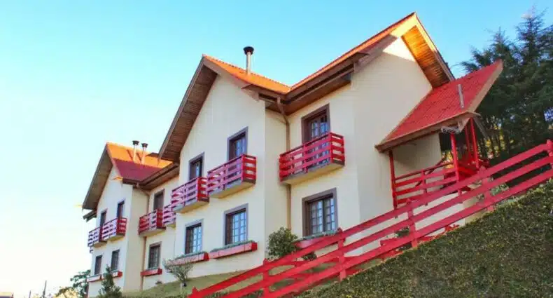 A Pousada AlpenRose, uma construção de dois andares em tom de bege com as sacadas pintadas em vermelho, para representar pousadas baratas em Campos do Jordão