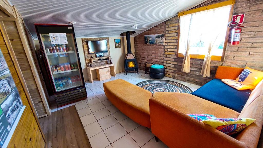 lounge da Pousada & Hostel Cape Town em Cambará do Sul com um sofá de canto laranja, uma máquina refrigeradora com bebidas no lado esquerdo e uma televisão ao lado da lareira ao fundo da sala