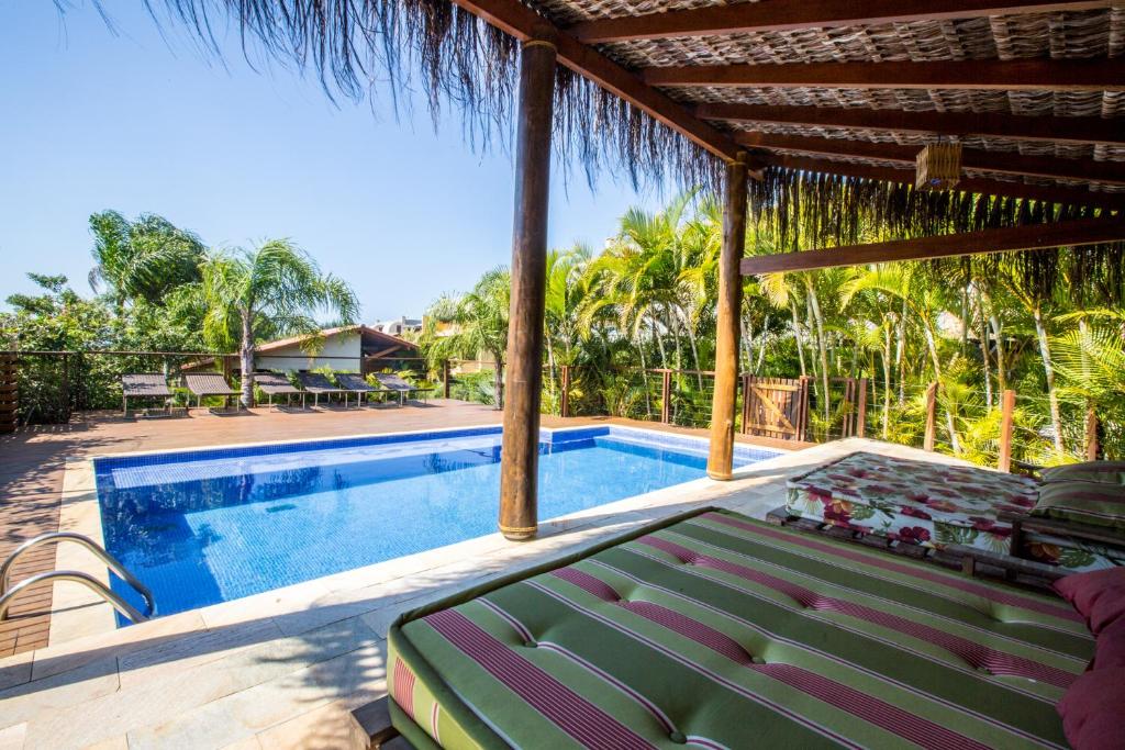 Piscina da Pousada Vila Tamarindo Eco Lodge com muito verde ao redor de toda a propriedade e, de um dos lados da piscina, há uma espécie de bangalô com sofás coloridos sob paletes de madeira
