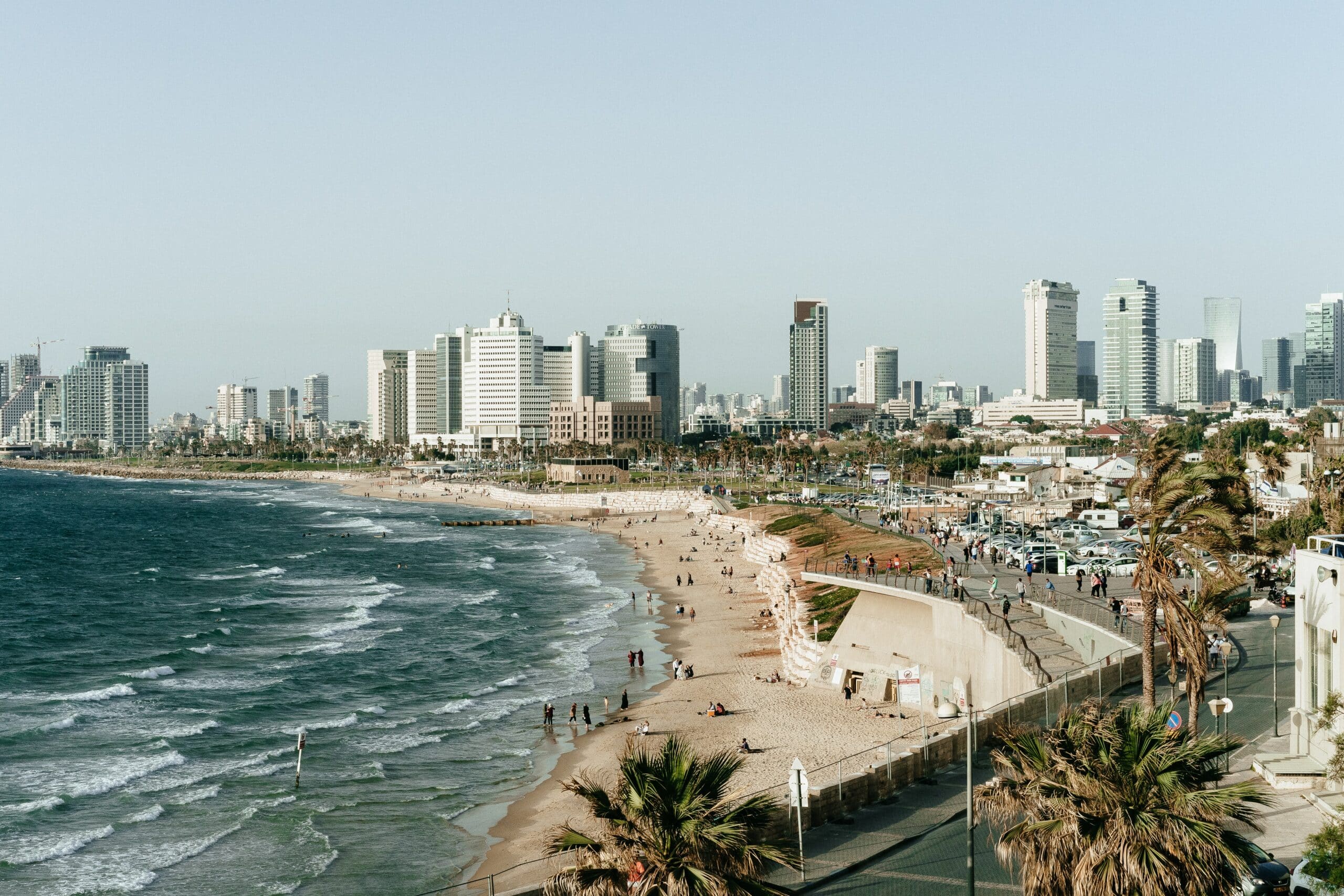 Vista de cima da cidade de Tel Aviv-Yafo, Israel, com mar, faixa de areia, pessoas caminhando na areia e ao fundo prédios.