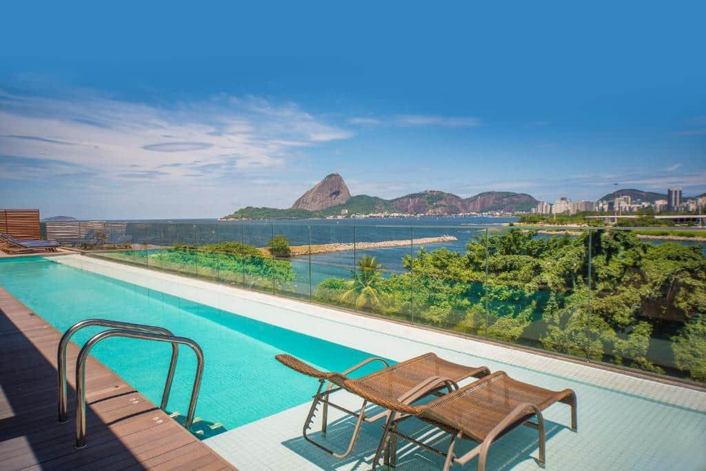 Piscina na cobertura do Prodigy Santos Dumont com uma bela vista da cidade do Rio de Janeiro e do mar, há algumas espreguiçadeiras pelo deck, para representar hotéis perto do Aeroporto Santos Dumont