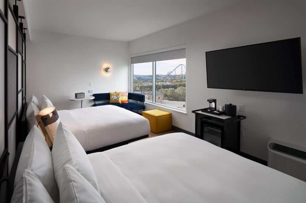 Quarto do Aloft Orlando International Drive com duas camas de casal, uma janela ampla com vista para um parque, há uma ampla televisão de frente para as camas, um pequeno sofá perto da janela e um ar-condicionado, para representar hotéis perto do SeaWorld