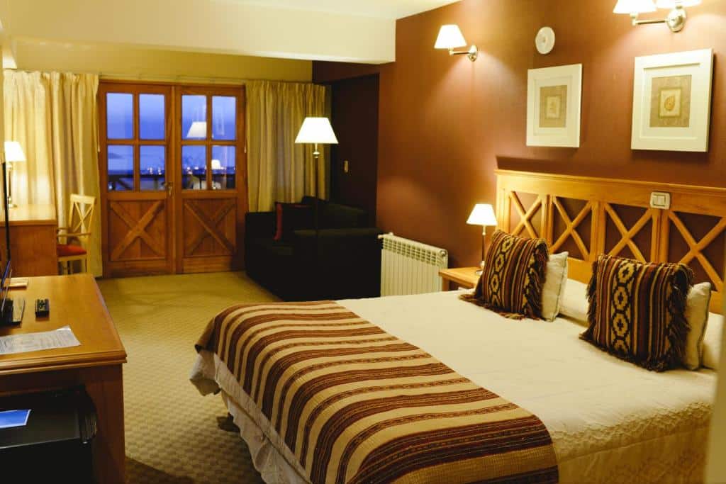 quarto amplo do Altos Ushuaia Hotel & Resto com uma cama de casal à direita, uma pequena área de estar com sofá e portas francesas para uma varanda