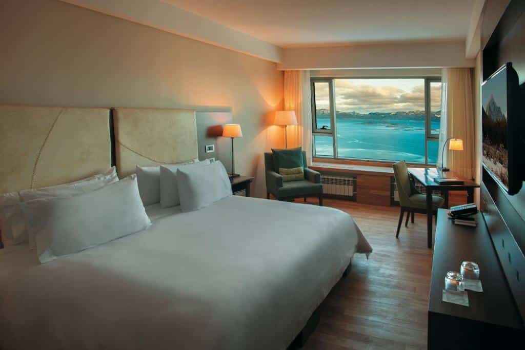quarto do Arakur Ushuaia Resort & Spa com uma cama de casal, uma poltrona e uma janela ampla com vista para o lago e as montanhas