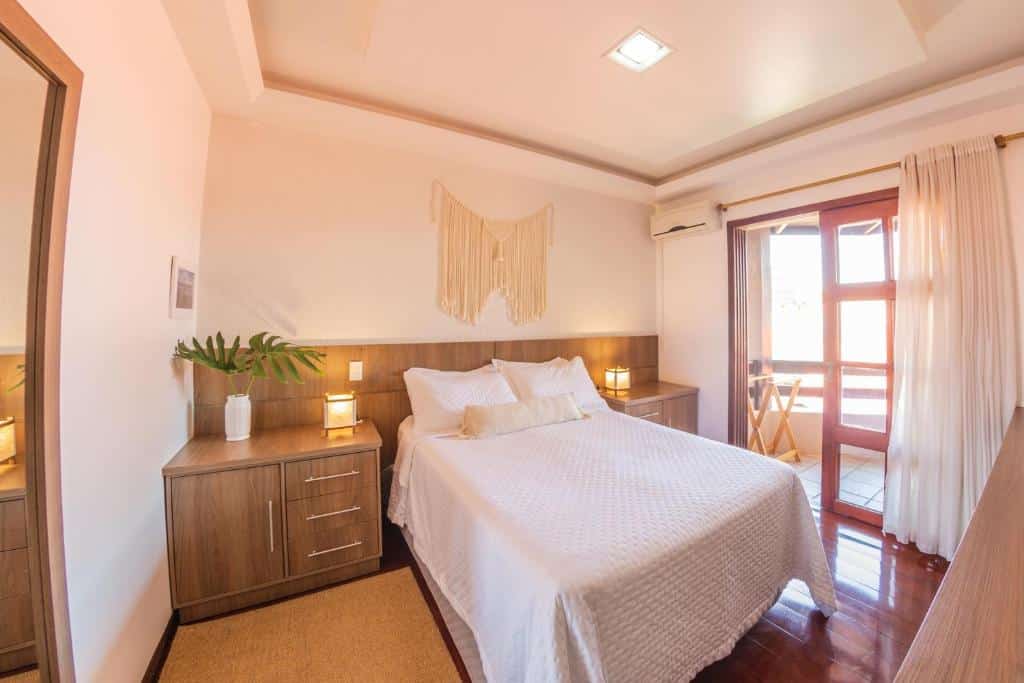 Quarto da Casa Mar Campeche com uma cama de casal, uma varanda com cortinas, um ar-condicionado de teto e dois pequenos móveis de madeira com gavetas nas duas laterais da cama