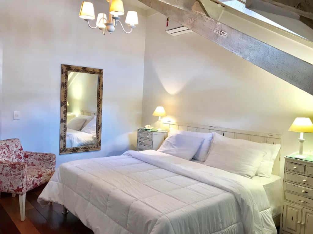 Quarto no Hotel Casablanca Imperial com uma cama de casal, um espelho, um lustre, uma poltrona e duas mesinhas de cabeceira com abajures