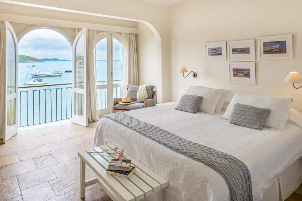 Quarto da Casas Brancas Boutique Hotel & Spa com uma cama de casal, uma sacada com duas portas com vista para o mar, uma poltrona e alguns itens de decoração pelo ambiente