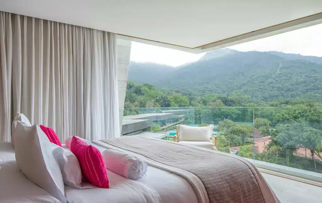 Quarto do Club Med Angra dos Reis com uma varanda aberta com vista direta para as montanhas cercadas de verde, do lado de dentro há uma cama de casal com travesseiros e almofadas, além de uma poltrona