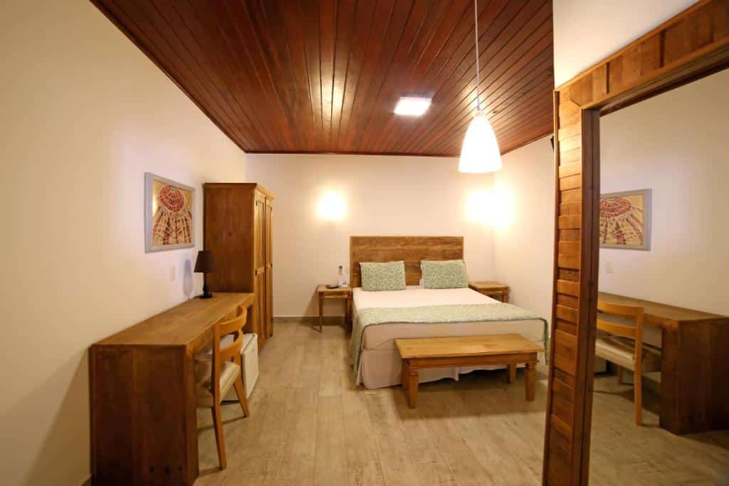 Quarto do  Coconut's Maresias Hotel com uma cama de casal, um armário de duas portas, uma bancada com uma cadeira, além de um espelho, tudo feito em madeira
