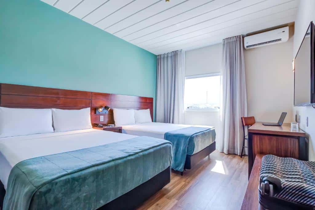Quarto do Cyan Resort by Atlantica com uma cama de casal, uma de solteiro, uma janela com cortinas, uma mesa para trabalha com uma cadeira e uma televisão
