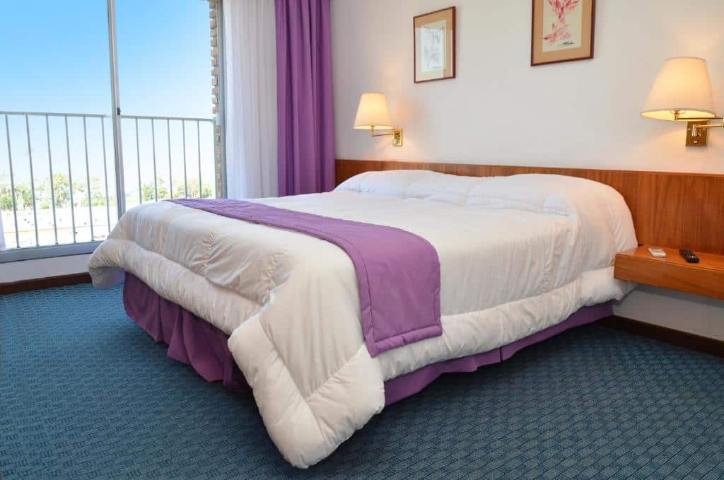 Quarto do El Mirador Hotel & Spa com cama de casal, duas mesinhas de cabeceira com abajures, uma varanda com vista, para representar hotéis em Colonia del Sacramento