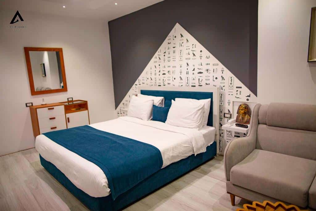 Quarto do Elite Pyramids Boutique com cama de casal com cobertas brancas e azuis, cômoda de madeira do lado esquerdo com espelho e poltrona bege do lado direito.