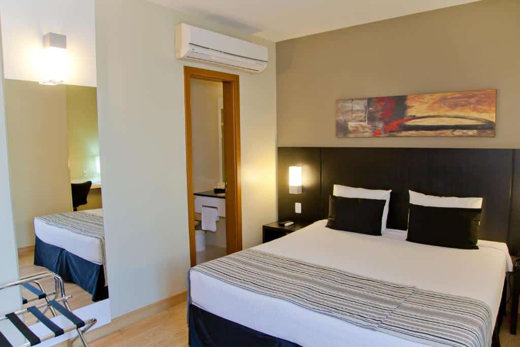 Quarto do Grande Hotel Petrópolis com uma cama de casal, uma cabeceira com luzes embutidas, um espelho e um ar-condicionado de teto