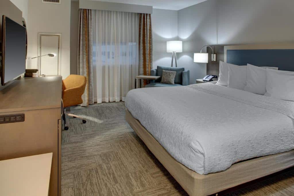 Piscina do Hampton Inn & Suites Miami Airport South/Blue Lagoon com cama de casal, poltrona do lado esquerdo, cômoda em frente a cama com TV.