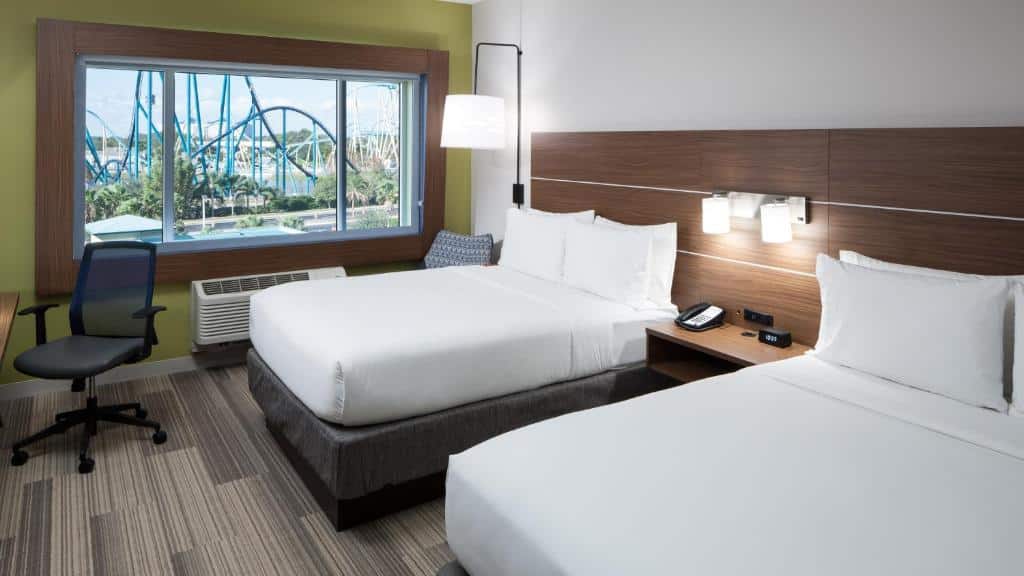 Quart do Holiday Inn Express & Suites - Orlando At Seaworld com uma duas camas de solteiro, uma janela ampla, chão de madeira, um abajur de teto e uma mesa de trabalho com uma cadeira giratória, para representar hotéis perto do SeaWorld