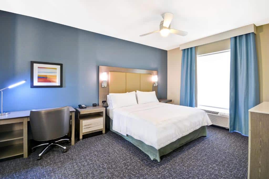 Quarto do Homewood Suites by Hilton Orlando Theme Parks com uma cama de casal, um ventilador de teto, uma janela ampla, uma mesa de escritório com cadeira e o chão é de carpete