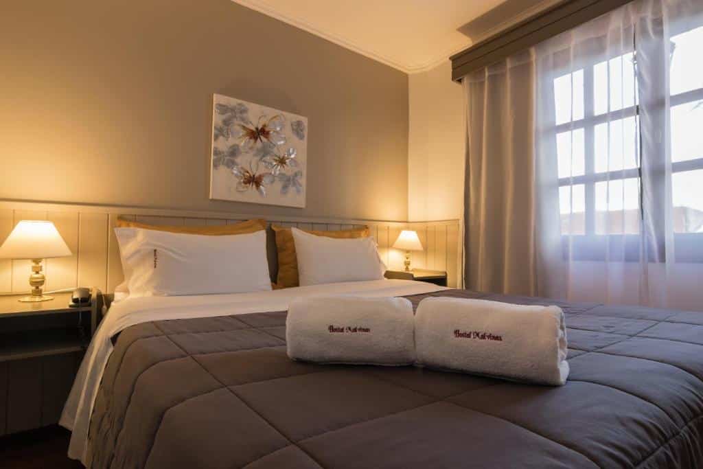 quarto da Hostería Hostal Malvinas com uma cama de casal e duas toalhas brancas em cima