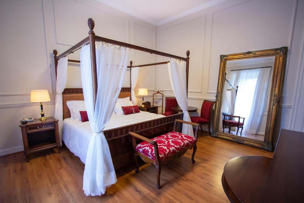 Quarto no Hotel Solar do Império com um amplo espelho com moldura de madeira, chão de madeira, uma cama de casal estilo bangalô, duas mesinhas de madeira com abajures