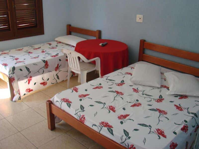 Quarto do Hotel Villagio D'Italia com uma cama de casal, uma de solteiro e uma mesa redonda com uma cadeira entre as duas camas