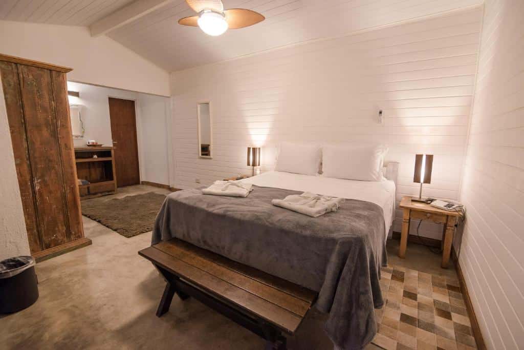 Quarto da Ilha de Toque Toque Boutique Hotel & Spa com cama ao centro do quarto, duas cômodas com luminárias e um banco ao pé da cama.