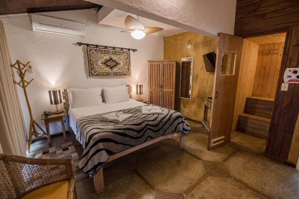 Quarto do Ilha de Toque Toque Boutique Hotel & Spa com acomodações rusticas, cama no centro do quarto, duas cômodas de madeira com luminária, cadeira do lado direito.