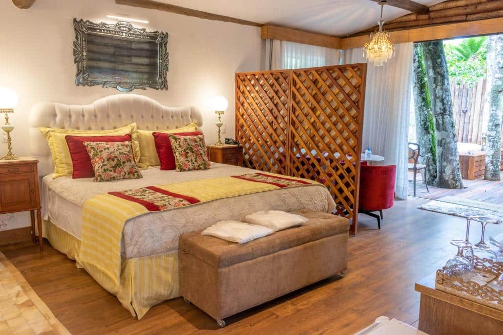 Quarto do Locanda della Mimosa com uma cama de casal, chão de madeira, varanda ampla com banheira de hidromassagem, um lustre e tudo decorado em estilo colonial com tons de vermelho e bege