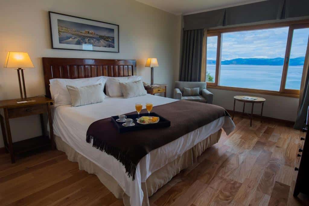 suíte do Los Cauquenes Resort com uma cama de casal, uma bandeja de café da manhã em cima da colcha e uma janela ampla com vista para a natureza no canto direito