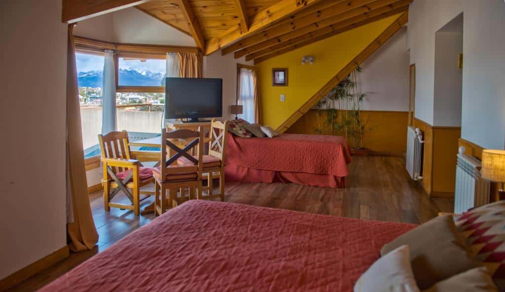 quarto do hotel Los Naranjos com duas camas de casal, uma janela ampla, decoração em madeira rústica e tons de amarelo e vermelho