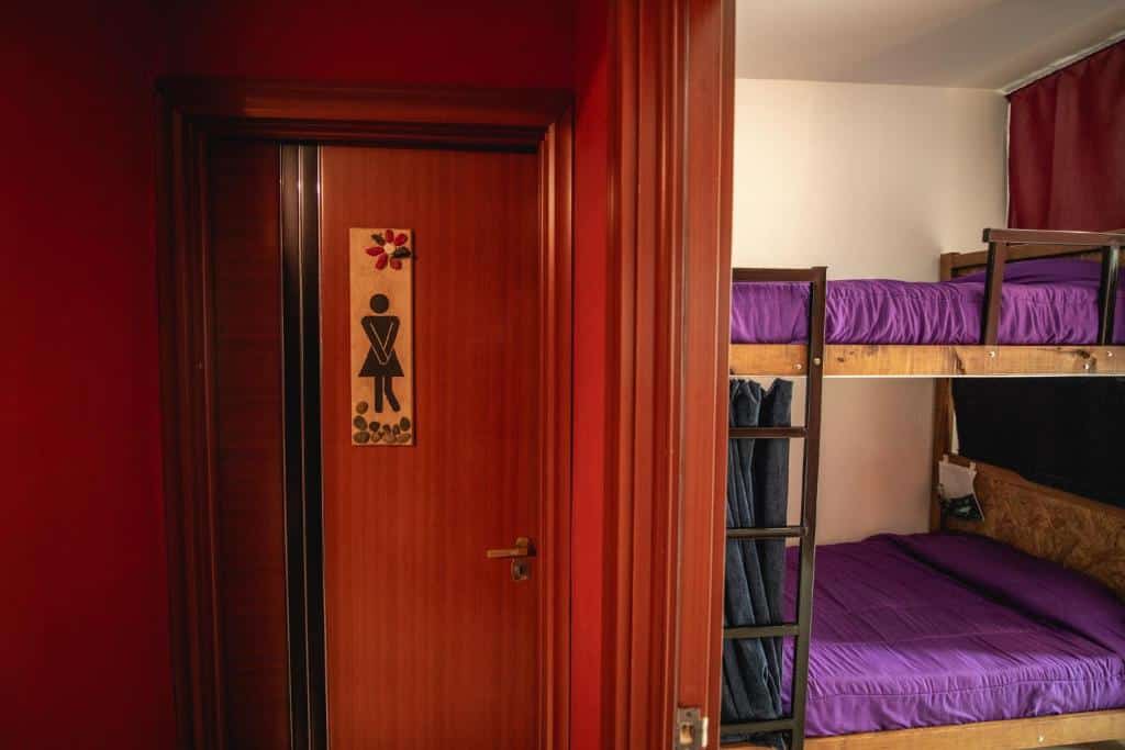 quarto feminino do Oshovia Hostel com uma beliche arrumada com lençóis violetas e um banheiro privativo