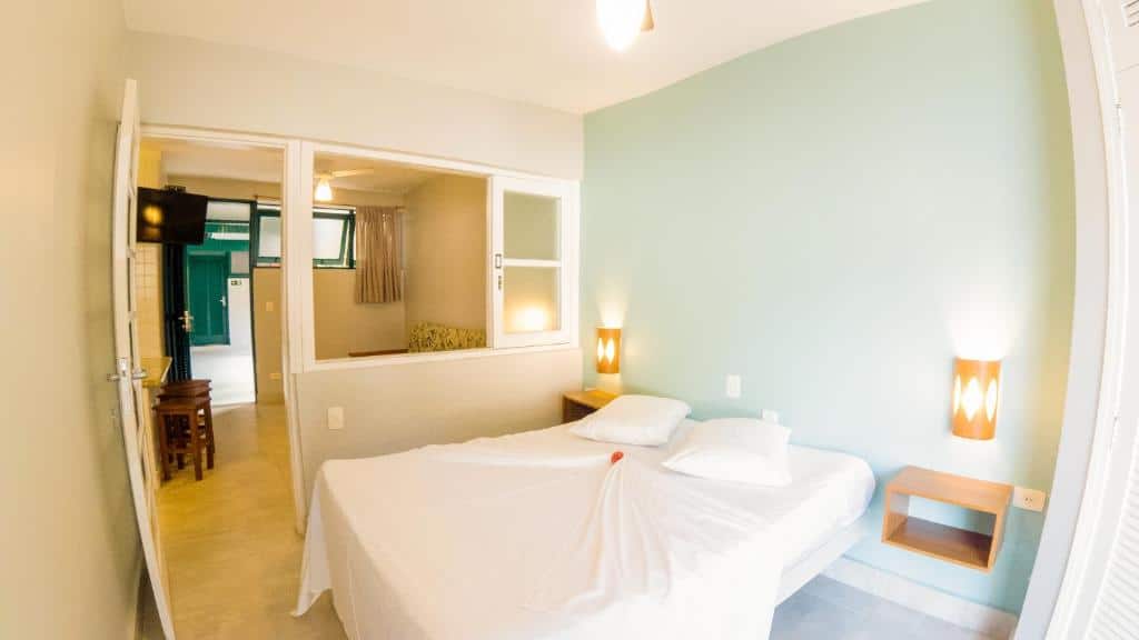 Quarto do Porto Paúba com cama de casal ao centro do quarto, duas cômodas com luminárias no lado da cama e porta do lado esquerdo e janela que dá acesso a uma sala de estar.